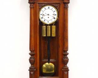 A 19th century Vienna Regulator wall clock retailed by Lechner Yozsef, Budapest. 8-day weight driven time and strike movement with quarter hour Grand Sonnerie chime, two-part porcelain dial with Roman numerals within a molded Brass bezel. Altdeutsch style Walnut case features a carved foliate crest over an arched door flanked by turned fluted pilasters with carved detail and shaped lower bracket. Older finish with minor wear, replaced crest, finials and some small moldings, dial hairlines, not running when cataloged. 58 1/2" high overall.