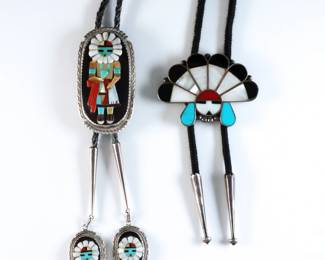Two vintage Zuni style Sterling Silver bolo ties. Both feature inlaid Turquoise, Mother of Pearl, Jet and Red Coral. Includes one Zuni with Kachina design by Beverly Etsate, and one Mexican made with headdress design. Zuni signed "Bev. Etsate / Zuni" at clasp and aiguillettes, tested Sterling, Mexican with partial "Sterling / 925 / AF" mark, aiguillettes tested Sterling. 3.62 troy ozs total. Some wear. Clasps up to 3" high, up to 20" long overall.