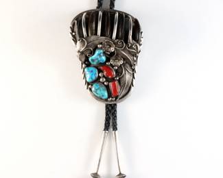 A vintage Native American Sterling Silver bolo tie with Bear Claw design. Features a paw shaped clasp with five incorporated Bear claws and bezel set Turquoise and Red Coral accents, on a braided leather tie. Marked "Sterling" and "FNG", aiguillettes tested Sterling. 4.57 troy ozs total. Some wear particularly to claws and leather tie. Clasp is 4" high, 22" long overall.