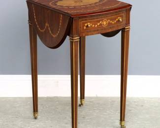 A Maitland Smith inlaid Pembroke table. Mixed wood construction with inlaid marquetry design featuring a molded, oval drop-leaf top and drawer on tall tapered legs with casters. "Maitland Smith" metal tag in drawer. Small glued repair to veneer at top, scrape to edge. 14 (30 1/2" open) x 18 1/2 x 27 1/4" high overall.