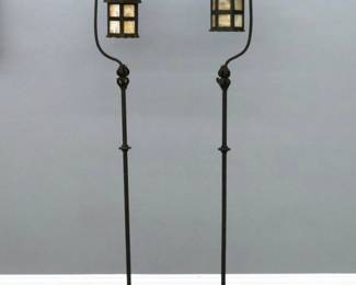 A pair of early 20th century Arts and Crafts floor lamps. Wrought Iron construction featuring a lantern form light with Carmel Slag Glass panels on a slender standard with cast floral decoration and tripod base with spade feet. Minor wear and some oxidation. Each 66" high.