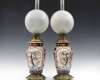 A pair of Japanese Imari oil lamps. Baluster form Imari porcelain vases with polychrome scenic and floral decoration with frosted globe shades on Bronze mounts. Minor surface wear. Vases are 10" high, 25 1/2" high overall with chimney.