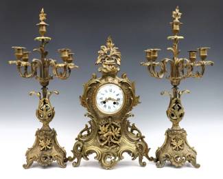 A turn of the century French three piece clock set by A. D. Mougin, Paris. 8-day time and strike movement, porcelain dial with Roman numerals and fancy filigree hands, serial #847877. Louis XV style Gilded Bronze case and matching five light candelabra. Some wear, running momentarily when cataloged. Up to 23 1/2" high overall.
