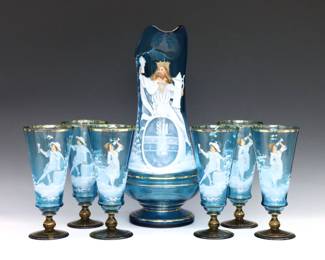 A seven piece late 19th century Mary Gregory Art Glass drink set. Blue and Amber glass with enameled figural court decoration and Gilded detail, includes a pitcher and six glasses. Minor surface wear, one glass ground at foot. Up to 14 1/4" high.
