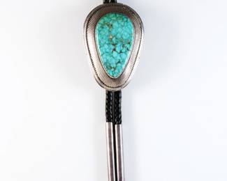 A vintage Navajo Sterling Silver bolo tie made by Howard Nelson. Features a teardrop form clasp with a large bezel set Turquoise and reeded detail on a braided leather tie. Marked "Sterling / Howard", aiguillettes tested Sterling. 5.06 troy ozs total. Minor wear. Clasp is 3 1/2" high, 21 1/2" long overall.