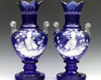 A pair of late 19th century Mary Gregory Art Glass vases. Baluster form in Cobalt Blue glass with flared sawtooth rim, clear handles and pedestal bases with enameled figural decoration with Gilded detail. Minor surface wear, rims with some fleabites and tiny flakes. 14" high.