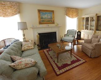 Stylish comfortable furniture including sofa, vintage French style carved arm chair in button back blue fabric, a china display cabinet, an upholstered skirted armchair, area rug, coffee table, oil paintings, lamps, clocks, vintage brass andirons and fire screen, and more