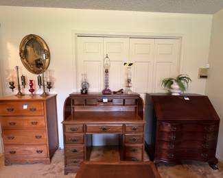 Rolltop desk in middle of picture with nine drawers. Other furniture is a 4 drawer chest on the left and a solid mahogany secretary desk with 4 drawers on the right. Oil lamps across the top of the furniture.