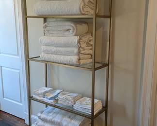 Contemporary brushed brass finish 4-shelf etagere, with assorted bed linens.