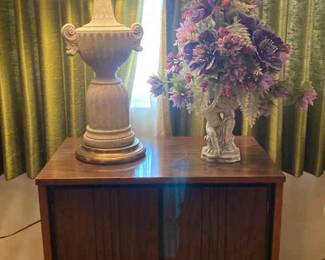 Two Shelf Cabinet Along With Lamp And Floral Decor
