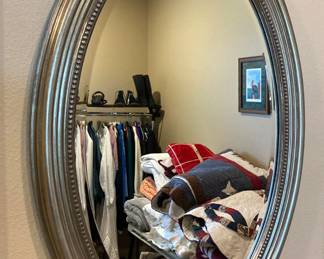 Oval mirror reflects quilts/blankets and a rack of women's clothes/shoes