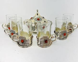 his stunning auction lot includes a silver-handled drinkware set featuring six glasses, a beautifully crafted sugar pot, and a decorative flower vase with glass blooms.