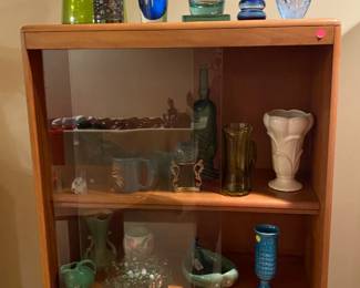 Cabinet full of pottery and glassware, topped with some art glass.