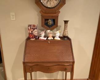 Nice drop front antique desk with antique wall clock in background.