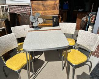 1950s (mid century) for my top chrome, legged kitchen table with four matching yellow white chairs. Three of the four chairs are in excellent condition. The one in the back has a slit in it. There’s also a small fan a trunk and a homemade toy box in the background.