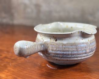 This lot features a studio pottery bowl, handmade by Blue Spruce Pottery in Bend, Oregon circa 1988. This item measures, 3.75” H x 7” W x 9.5” D. Michael and Michele Gwinup established Blue Spruce Pottery in Bend Oregon in 1976. Their stoneware pottery are all functional pieces that are food safe. It is fired in a gas kiln to 2200 degrees, cone 10. This makes the clay very durable. Maker mark underneath as shown in photos.