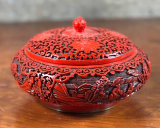 This lot features a vintage Chinese lacquered red Cinnabar jar, circa 1970s. This piece measures, 4” H x 8” W x 8” D. A cinnabar jar is a decorative Chinese art piece, often a ginger jar or vase, that features a red lacquer finish, typically carved with intricate designs. The “cinnabar” in this case refers to the red lacquer itself, not the mineral cinnabar (mercury sulfide). The lacquer is applied in multiple layers and then carved to reveal the underlying designs.