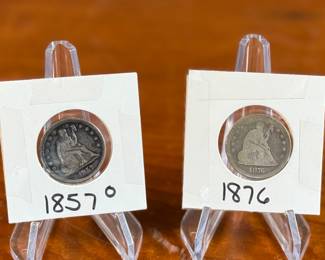 A pair of silver seated liberty quarters. One is a 1857-O and the other is 1876. Both have been kept in protective slips. Robert Ball Hughes and Christian Gobrecht designed the Liberty Seated Quarter. They were minted from 1838 to 1891. The Liberty Seated design became one of the longest-running motifs in the United States coinage. Until 1891, U.S. quarters were 90% silver and 10% copper.