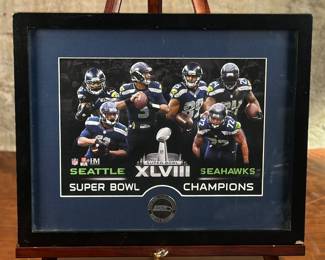 This lot features framed memorabilia of the Seattle Seahawks celebrating winning Super Bowl XLVIII. This item measures in the frame, 12” H x 15” W. In Super Bowl XLVIII, the Seattle Seahawks defeated the Denver Broncos with a score of 43-8. This victory marked the first Super Bowl championship for the Seahawks. The game was played at MetLife Stadium in East Rutherford, New Jersey, on February 2, 2014.