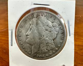 This lot features a 1904-S Morgan Dollar. The Morgan silver dollar, designed by Mint Chief Engraver George T. Morgan and produced from 1878 to 1904, with a brief reissue in 1921, was a significant part of American coinage. It was minted as a standard silver dollar after the Coinage Act of 1873 ended the free coining of silver. The Morgan dollar, known for its size and weight, became a popular coin, especially in the American West, and is now a favorite among collectors.