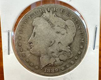 This lot features a 1889-O Morgan Dollar. The Morgan silver dollar, designed by Mint Chief Engraver George T. Morgan and produced from 1878 to 1904, with a brief reissue in 1921, was a significant part of American coinage. It was minted as a standard silver dollar after the Coinage Act of 1873 ended the free coining of silver. The Morgan dollar, known for its size and weight, became a popular coin, especially in the American West, and is now a favorite among collectors.