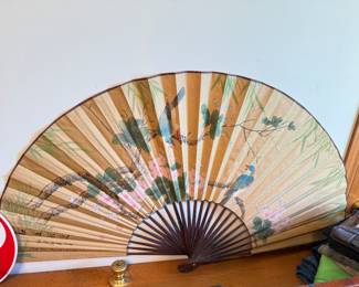 Large vintage hand-painted Asian folding wall fan featuring delicate cherry blossoms, bamboo, and two vibrant birds perched on a flowering tree branch. The artwork is set against a warm tan background with deep brown wooden ribs and trim. Signature of artist on right.  This striking decorative fan measures approximately 60 inches wide when open and makes a beautiful statement piece for any wall.