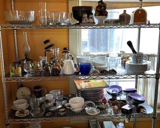 Lots of kitchen wares including French press coffee makers, tartlet pans, ravioli press, cups and saucers, stacks of plates and dishes, baking pans, serving bowls, salt and pepper shakers, bar ware, large stainless steel lidded serving dishes, and more