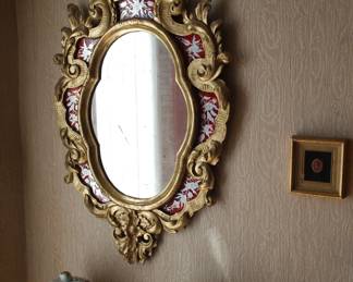 An antique carved gilt wood oval mirror with seven silver flowered eglomisé panels with red backgrounds, the top adorned with a carved Georgian style floral urn