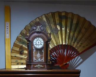 Antique Triumph Clock                                                                                             Wood case; side mirrors with wood finials; original keys and pendulum; 2 ft  H; 17 in. W; 6 in. D         Chinese Fan Wall Décor                                                              40” H; 69” W
