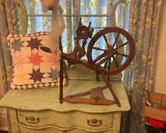 Small antique wooden spinning wheeloo sitting on a shabby painted serpentine wash stand and handmade quilted pillow cover