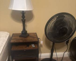 Nightstand w electrical outlet on side. Floor fan and lamp