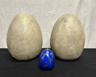 Two large grey decorative eggs, believed to be resin. One small ceramic blue egg with gold colored detailing.