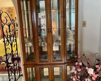 Narrow, tall, beveled glass doors curio cabinet. Lighting inside. There is also a short one to match. Inside the cabinet is a shelf filled with Precious Moment statues.