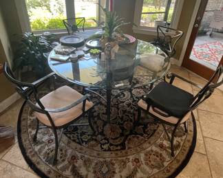 Glass top round table with 4 iron arm chairs. Round oriental rug. Assortment of placemats
