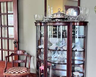 curved glass china cabinet filled with crystal and silver-plate items