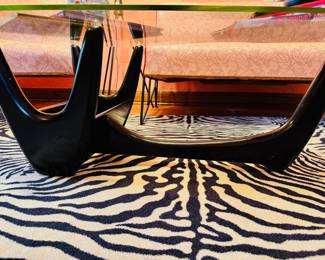 Amazing 1950’s biomorphic glass top coffee table with black wood book storage base. There are some small chips to the glass
