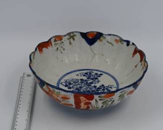 A rare and early Japanese Imari porcelain bowl with a scalloped rim, decorated with a central underglaze blue floral medallion and sparse overglaze enamels in iron red and green. The bowl shows traditional hand-thrown construction with visible kiln pitting and firing marks typical of early Edo-period production. Estimated date: 1800–1830