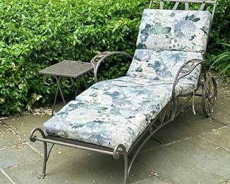 (2pc) Wrought Iron Chaise Lounge & Side Table | Wrought iron outdoor/patio furniture, including a small rectangular side table and a chaise lounge chair on wheels with floral design along the top edge. Similar to Woodard Furniture designs. Includes cushions. - h. 17.5 x w. 12.5 x l. 14.5 in