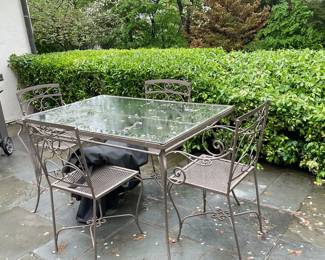 (5pc) Wrought Iron Dining Table & Chairs - Square | Wrought iron outdoor/patio furniture, including a square dining table with glass table top insert, two (2) armchairs and two (2) side chairs (no arms) with floral design along the top edge. Similar to Woodard Furniture designs. Chairs include cushions. Side chairs: h. 33.5 x w. 16 x d. 15. Armchairs: h. 33 x w. 23.5 x d. 18 - h. 28.5 x w. 32 x l. 48 in (Table)