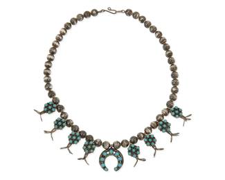 327
A Navajo sterling silver and turquoise squash blossom necklace
Mid/late 20th century
Unmarked
A diminutive necklace with a small central naja with set turquoise, and with eight cluster-set turquoise blossoms, all strung on a strand of silver beads
17" L x 1.125" H
53.1 grams gross
Estimate: $600 - $800