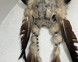 Engraved and painted cow skull with fur, feathers and beads.