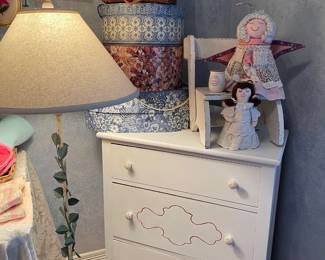 White pained chest of drawers, hat boxes, handmade angels, and metal floor lamp with leaf decoration