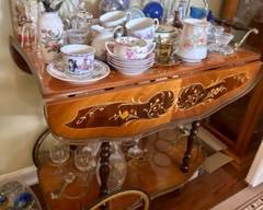 Vintage Italian lacquered two-tier, drop leaf dessert/bar cart trolley featuring hand inlaid marquetry style floral design and brass hardware including bottle holders - purchased in Germany. Excellent condition for its age (1920-1950). Wide variety of tea cups and saucers from England and Germany. Dimensions: 29w x 16d x 28h; $875.00