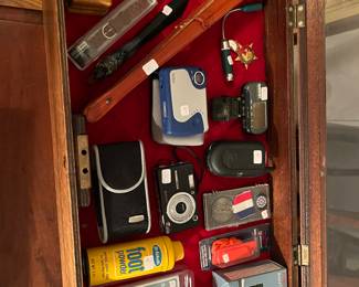 Speedy charger, vintage tin Dr. Scholl’s, foot powder can, security whistle, Kodak digital easy share camera, Vintage vivitar camera, Oriental fan, flip phone, Wooden carved duck letter opener, Vintage trinket box, Race car cigarette lighter holder and Garmin armband GPS.