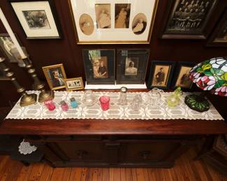 Vintage brass candlestick holders, framed antique photographs, crocheted table runner, salt and pepper shakers, sugar shaker, vaseline glass "thousand eye" pattern cut glass cruet, and stained glass table lamp