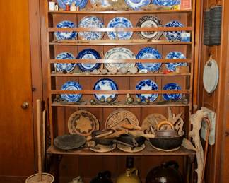 Vintage tins and boxes; shelving unit with flow blue china; Antique and vintage cast iron cooking pans, vintage primitive carved kitchen tools and household tools, a collection of antique pottery jugs; vintage primitive wrought iron skillets, griddle and three-legged long handled pot; vintage Native American woven bowl/basket