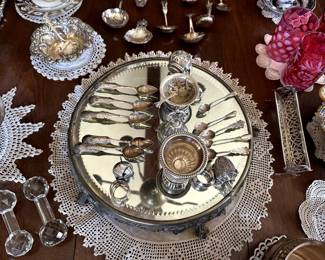 A silver footed mirrored circular centerpiece / tray showing just some of the beautiful antique sterling silver and coin silver items available - tea infusers, spoons, salt cellars with spoons, olive spears, sugar cube tray, tea strainers, bowls and compotes.