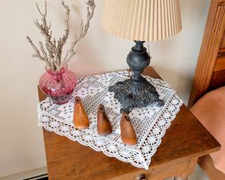 Closer view of vintage/antique side table, three antique primitive wooden shoe forms or lasts, child sized; antique cast iron table lamp, cranberry colored glass vase, and an antique 19th century cast iron lion doorstop