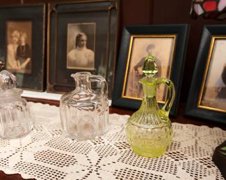 Closer view of the crocheted table runner, framed antique photographs, and vintage vaseline glass "thousand eye" patterned glass stoppered cruet
