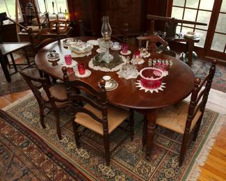 Another view of the beautiful extendable wooden dining table and antique ladderback and cane seat chairs, vintage area rugs/carpets, a Swedish monk chair, antique primitive fruit press